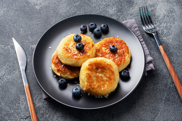 Fritters of cottage cheese with blueberries. Cheese curd cheesecakes, pancakes on a dark concrete background. Copy space.