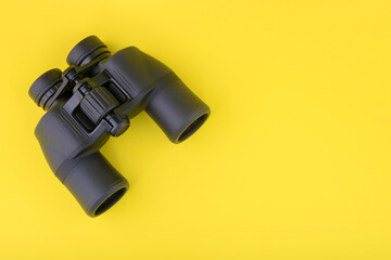 Binoculars on yellow background top view