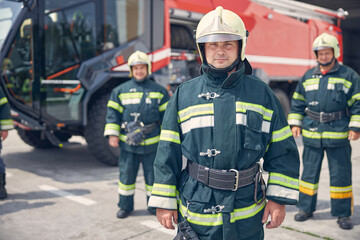 Three handsome professional firefighters in helmets standing in the outdoors