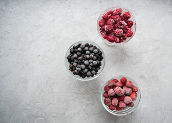 Frozen berries: currants, raspberries and strawberries in bowls on a gray background. Image with copy space, top view, vertical orientation.