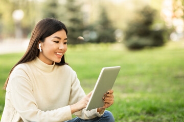 Fototapeta premium Female asian student using tablet, sitting in the park