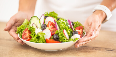 Vegetable salad in white dish holding woman hands