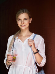 Outdoor summer city lifestyle portrait of young trendy dressed blonde happy woman with lemonade drink having fun outdoor in the city ready for travel