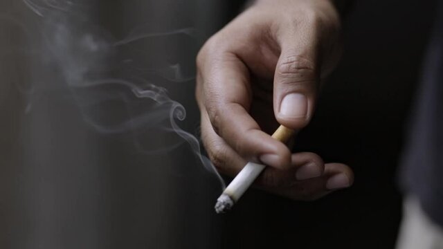 close up man holding smoking a cigarette in hand. smoke spread. dark background.