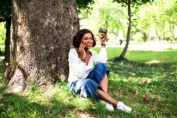 Beautiful african woman talking by phone and sitting on the grass.