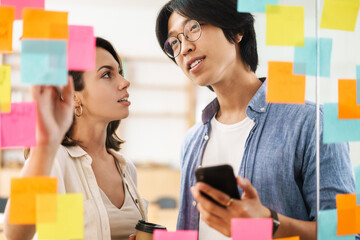 Image of multinational pleased colleagues using mobile phone and talking
