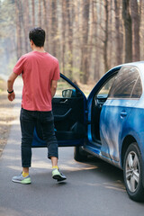 Handsome man standing on the road near opened door of his car.