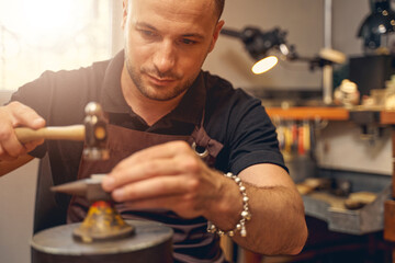 Serious metalsmith treating a workpiece placed on the anvil