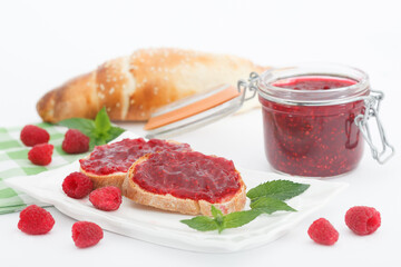 Raspberry jam with fresh raspberries and bread slices on white background. Homemade marmalade, perfect for light, sweet breakfast.