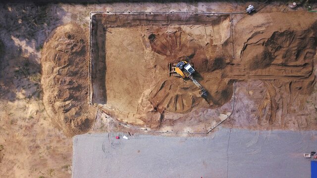 Bagger auf einer Baustelle hebt einen Keller aus. Tiefbau, Erdbau, Auskoffern aus der Vogelperspektive