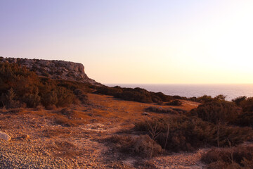Fototapeta na wymiar View from below on the red stony soil and Cape Cavo Greco (Capo Greco) in the sunset. Cyprus.
