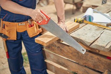 Joiner sawing off a piece of wooden bar - obrazy, fototapety, plakaty