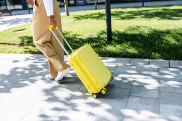 Female hands pull a yellow trolley bag outdoors. No faces visible. Travel time