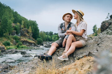Happy young couple travelers in casual outfits kissing on mountain river background. Local tourism, weekend trip concept