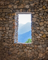 view to distant mountains from old window frame on rough stone wall
