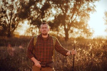 Irish looking red bearded hunter in checkered shirt staying outdoors in the sunset light and holding his gun