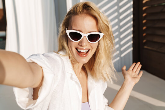 Image of happy woman in sunglasses smiling while taking selfie photo