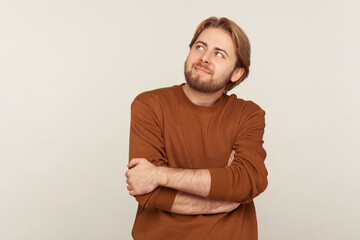 Portrait of happy inspired man with beard wearing sweatshirt looking up with pensive expression, dreaming pleasant thoughts, fantasizing ang and making wish. studio shot isolated on gray background