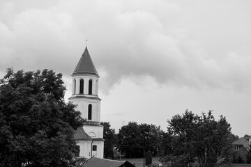 A black and white photo of a white tower of a nearby Catholic church located in the middle of a...