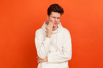 Unhappy young man in casual style sweatshirt with hood suffering from terrible toothache, gingival...