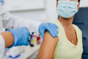 Female doctor or nurse giving shot or vaccine to a patient's shoulder. Vaccination and prevention against flu or virus pandemic. - obrazy, fototapety, plakaty