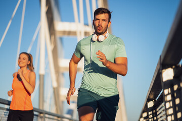 Young couple is jogging on bridge in the city.