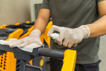 Hands of man using spraying alcohol antiseptic,disinfecting spray, cleaning on shopping cart, trolley handle, protection during Coronavirus pandemic,Covid-19.