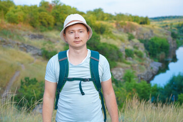 a guy in a t-shirt and with a backpack goes traveling through the mountains of the canyon and looks at the sunset