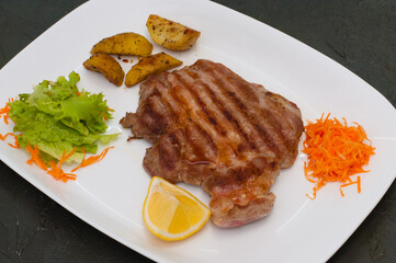 Grilled meat steak with lemon, carrots, lettuce and potatoes. Juicy and very tasty dish of Italian cuisine
