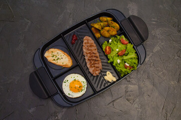 Breakfast, fried steak or cutlet, salad with tomato and green vegetables, croutons, potatoes, egg , view from the top, dark background. Concept healthy eating, diet, menu, nutritious food.