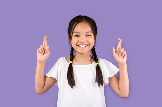 Asian Kid Girl Keeping Fingers Crossed Posing Over Purple Background