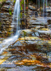 Silky water flowing over coolorful rock strata with moss