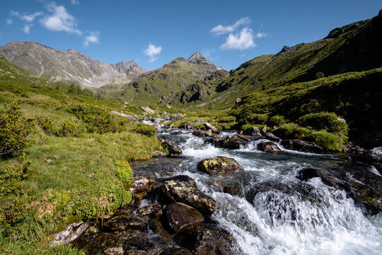 Bergbach (Debantbach bei Lienz) in &Ouml;sterreich mit Steinen und gr&uuml;nen Wiesen, im Hintergrund hohe Berge (Gl&ouml;dis, Debantgrad, Hochschober, Nationalpark hohe Tauern)