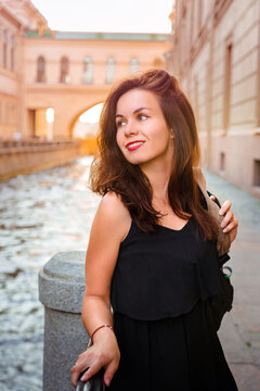 Vertical portrait of a young woman with long hair in a dress against the background of the canal in St. Petersburg on a summer day at sunset