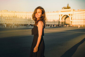 Fototapeta premium A young woman in a dress with long hair walks on Palace square at sunset in Saint Petersburg