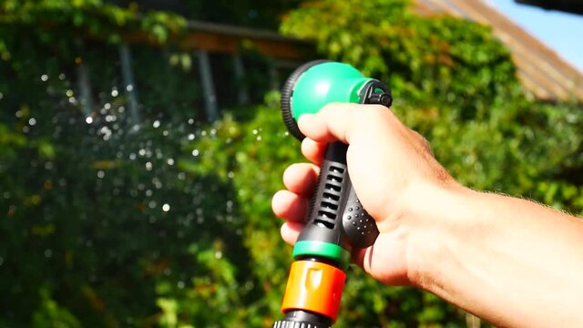 Close up of a mans hand holding a watering spray and watering the garden