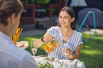 Happy smiling female wearing blouse pouring orange lemonade in glass
