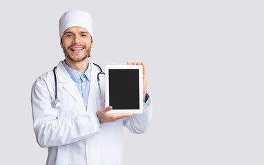 Positive young doctor showing digital tablet with blank screen