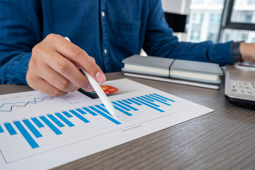 A businessman or accountant is sitting holding a pen to check the company's profit chart, the concept of growth planning in long-term investments.