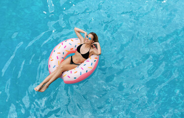 Seductive Caucasian girl in bikini swimming on inflatable ring in pool, overhead view. Blank space