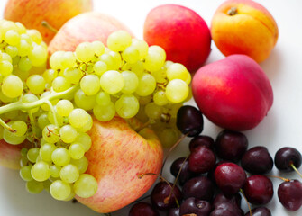 a set of fruits, a bunch of yellow quiche-mish grapes lies on ripe apples, next to cherries and peaches on a light surface. Natural fruit dessert. A tasty, healthy snack, a slice of summer, a harvest.