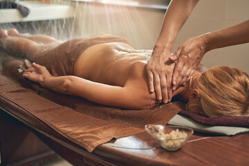 Massage therapist female masseur doing shoulder massage for female customer in spa center