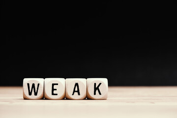 Social topic "Weak" written on wooden cubes with dark background