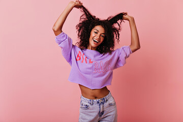 Sensual black girl posing on rosy background with happy face expression. Jocund african woman...