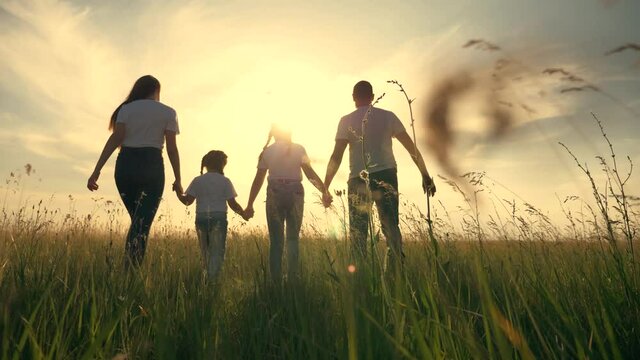 Happy family together. People hold hands on a walk on the green grass. The concept of teamwork. Happy father with daughters.