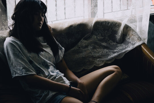 Asian Girl Sitting With Absent Mind On The Sofa By The Window.