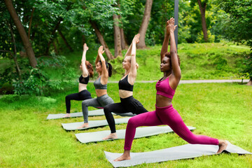 Multinational young girls practicing yoga outdoors, standing in warrior pose at park. Free space
