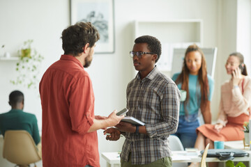 Side view portrait of agitated manager instructing young African-American man while standing in office, copy space