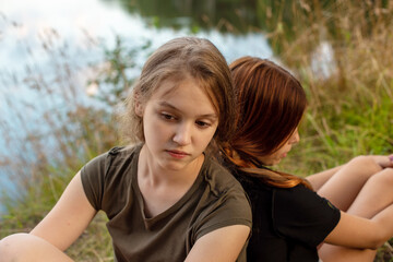 two teenage girls are braided in one braid on a picturesque river bank, the concept of friendship and the ability to find a compromise