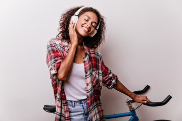 Pleasant black girl enjoying music with eyes closed. Appealing african lady listening favorite song during photoshoot with bicycle.